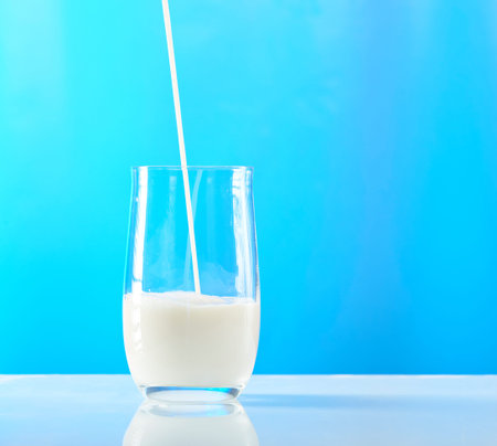 pouring milk in glass isolated on blue backgroundの写真素材