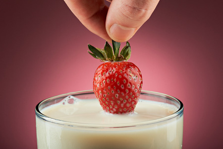 adding strawberry into milkshake isolated on pinkの写真素材