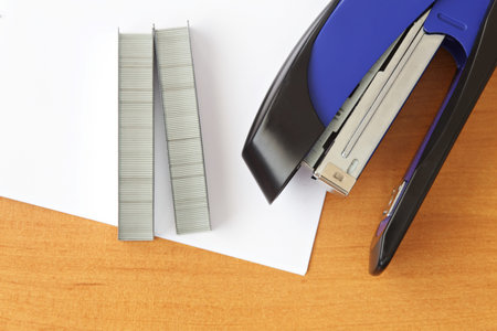 Blue stapler and staples with paper on wood table