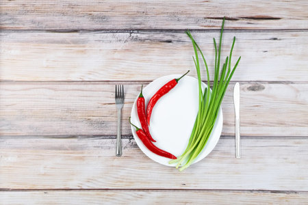Red hot chilli pepper and scallions on white plate wooden background