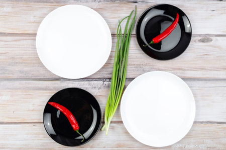 Red hot chilli pepper and scallions on black plate on wooden background