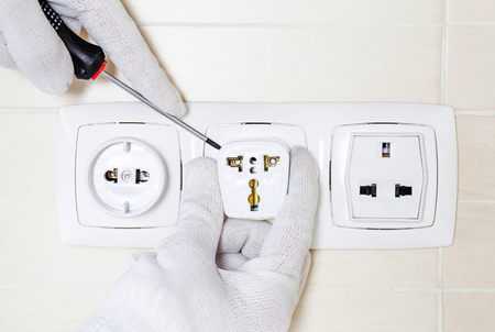 Electrician repairing socket with screwdriver. Hands in white protective gloves.の写真素材
