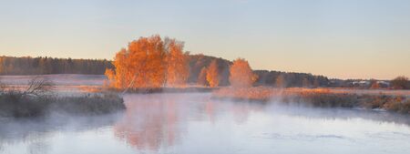 Panoramic landscape of autumn sunrise. trees reflect in lake. Misty autumn morning.の写真素材