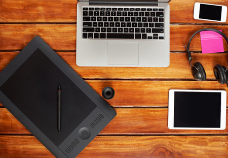 Gadgets of retoucher on brown wooden table. Modern laptop, tablet, smartphone, headphones view from...