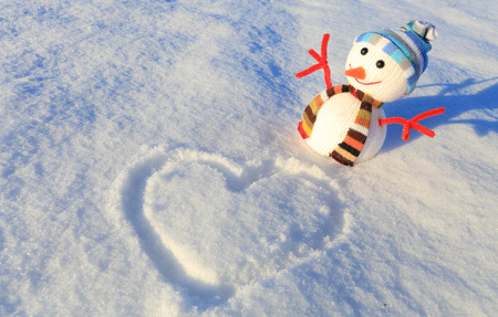 Small snowman on snow. Beautiful valentines day background. Heart drawing on white snow.の写真素材