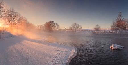 Winter sun shine through mist. Bright sunbeams illuminate white snow and ice. Sunny winter background. Frosty winter morning on river.の写真素材