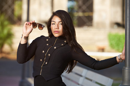 young hispanic woman hold sunglasses on day urban background