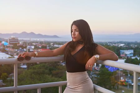 Brunette young woman in dress outside city sunset backgroundの写真素材