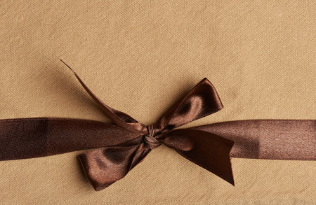 Brown ribbon on yellow fabric cloth background close up