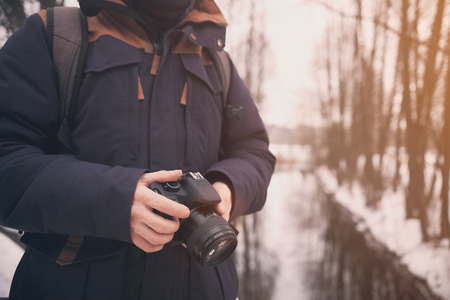 Man with camera close uo. Closeup of hand with camera. Photographer on sunny winter background. Lifestyle travel concept in vintage colors.の写真素材