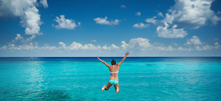 Happy woman jump to caribbean sea in blue sky background. Holiday in tropical resortの写真素材