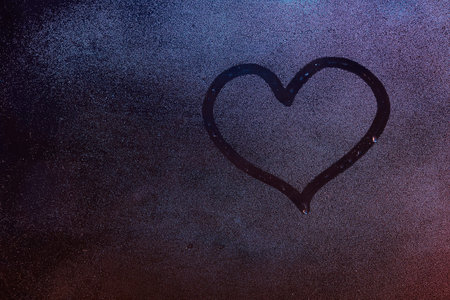 Heart shape drawing on fog window background. Heart symbol on wet window glass