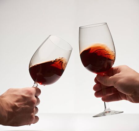 Happy cheers with two red wine glasses isolated on white background. Toast closeup with red wineの写真素材