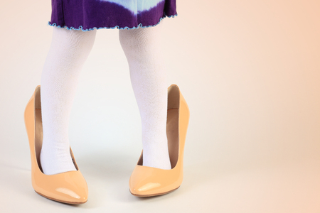 Child trying on high heel shoes. Close-up of child feet in yellow shoes. Little girl play with mother's shoes. Funny child background.の写真素材