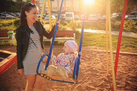 Happy family scene. Mother brunette and kid enjoing swing. Young mother playing with kid in the evening.の写真素材