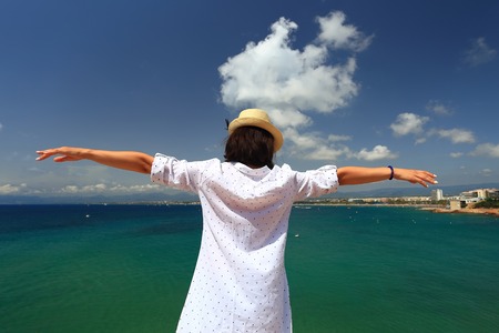 Woman with hands wide open on the mediterranean sea background. Girl in summer hat and white shirt at spanish resort.の写真素材