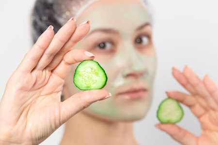 Woman with green cucumber mask on face holding round slices of cucumber. Facial skin care with natural mask. Healthy lifestyle background.の写真素材