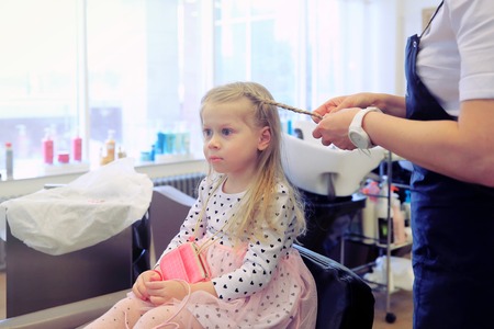 Little girl in barbershop. Making hairstyle for toddler in professional barbershop.の写真素材