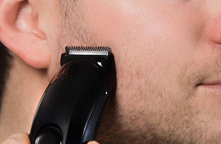 Trimmer on unshaven face closeup. Man shaving with electric shaver.の写真素材