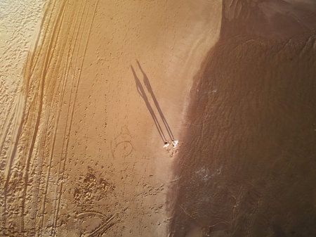 Above view on two people standing on beach in sunset yellow lightの写真素材