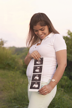 Happy smiling pregnant woman with ultrasound print on nature backgroundの写真素材