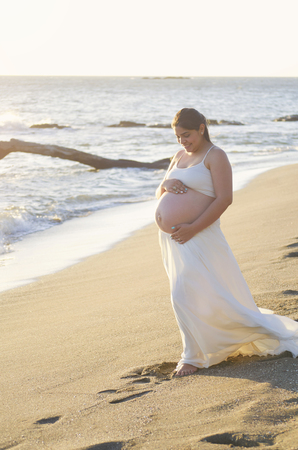 Happy smiling pregnant woman stand on beach sunny backgroundの写真素材