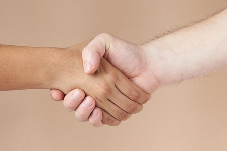 Black and white skin people handshake isolated on brown backgroundの写真素材