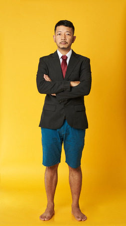 Asian business man in shorts with crossed arms isolated on yellow backgroundの写真素材