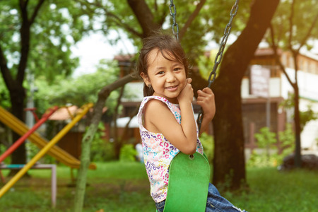Portrait of asian small girl sitting on swings in sunny park backgroundの写真素材