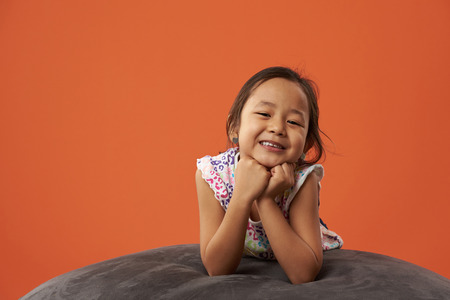 Pretty asian girl portrait lay on soft sofa isolated on orange color backgroundの写真素材