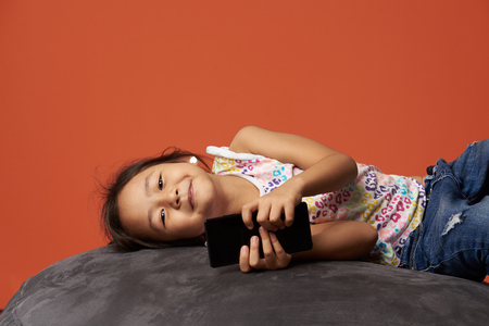 Asian girl lay on sofa with smartphone in orange color backgroundの写真素材