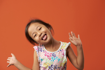 Portrait funny asian girl with tongue out isolated on orange backgroundの写真素材