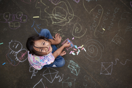 Asian small girl with chalk on painted asphalt background above top viewの写真素材