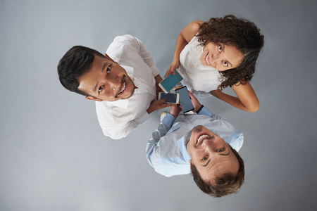 Three young people with smartphones smiling to camera isolated on gray background above top viewの写真素材