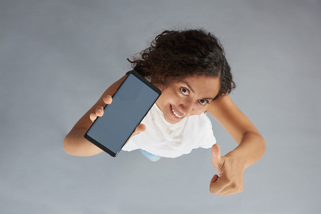 Smartphone in woman with dark curly hair hand above top view showing thumb upの写真素材