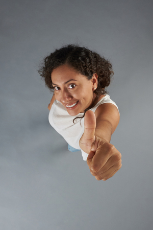 Thumb up showing young woman with dark curly hair isolated on gray background above top viewの写真素材