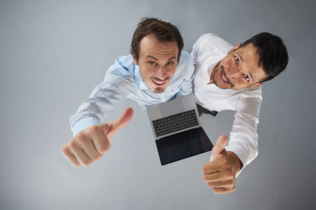 Two man with laptop showing thumb up isolated on gray background above top viewの写真素材