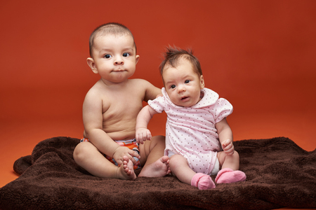 Two small baby kids portrait sitting on blanket isolated on orange color backgroundの写真素材