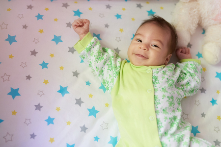 Happy baby girl laying on bed with hands upの写真素材