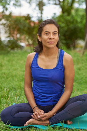 Young woman sit on yoga mat in natural summer park background