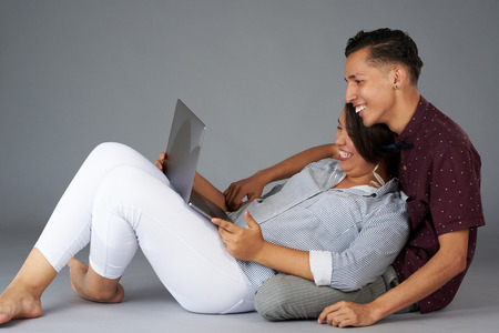 Latin couple watching movie on laptop isolated on gray studio backgroundの写真素材