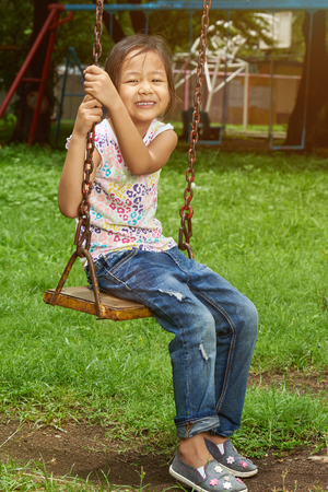 Portrait of active asian girl sitting in park swingsの写真素材