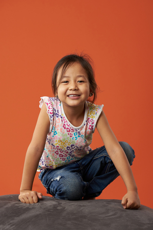 Portrait of asian girl smiling sit on sofa isolated in orange backgroundの写真素材
