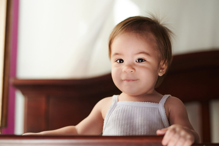 Portrait of adorable baby girl standing on cribの写真素材