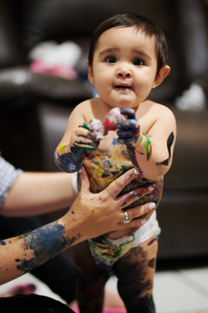 Dirty baby girl with colorful paint playing in houseの写真素材