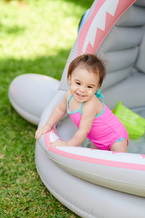 Happy smiling baby girl stay in swimming pool on sunny backyardの写真素材