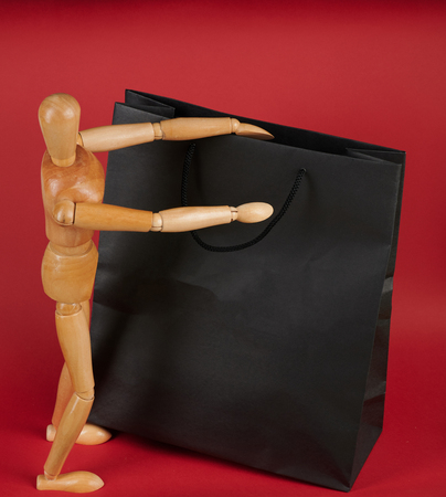 Man with big shopping bag. Wooden doll opening black paper bagの写真素材