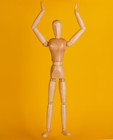 Wooden man toy with hand up isolated on yellow backgroundの写真素材