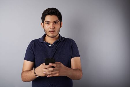 Surprised face of young man holding smartphone in handsの写真素材