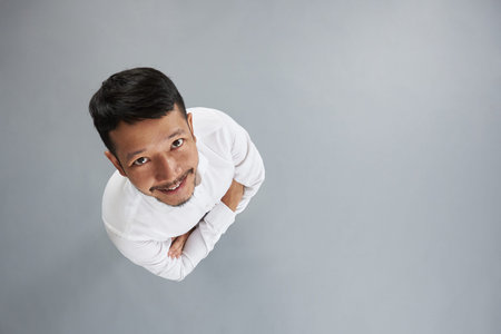 Young asian man with crossed arms isolated on gray background above top viewの写真素材